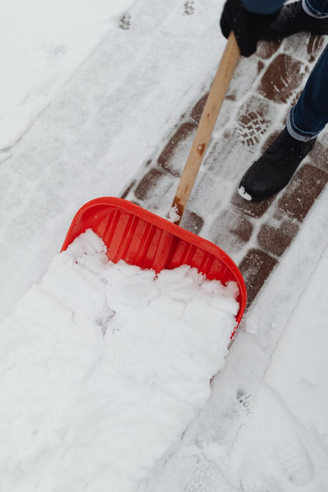 Schnee wird mit einer roten Schaufel vom Weg geräumt